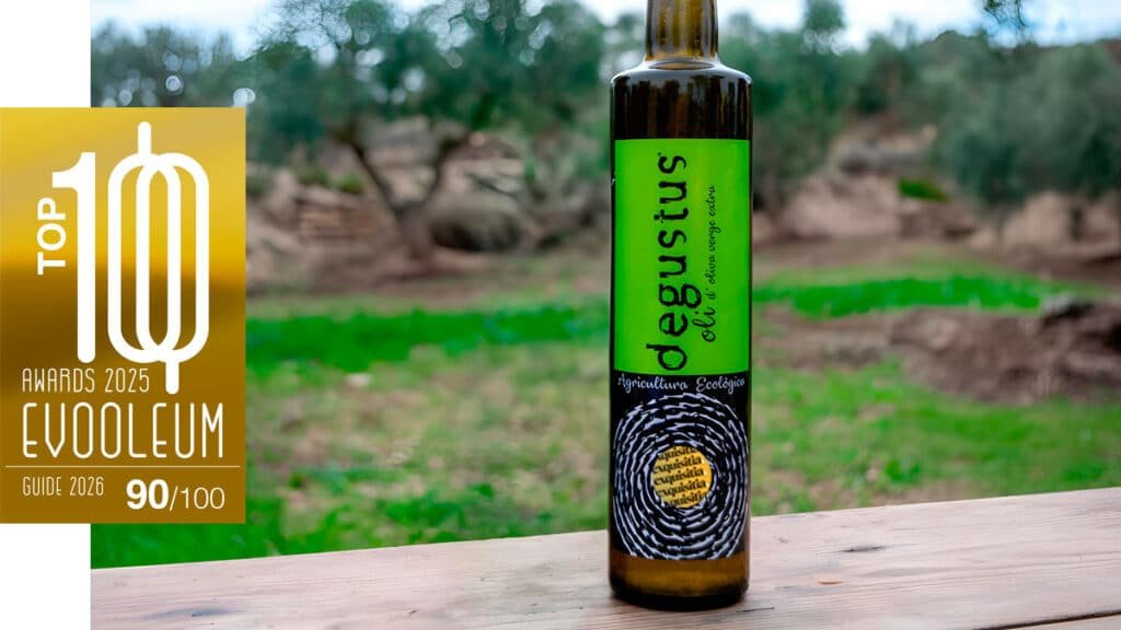 Botella de aceite Degustus Ecológico premiada en el EVOOLEUM TOP100, en un olivar de Lleida